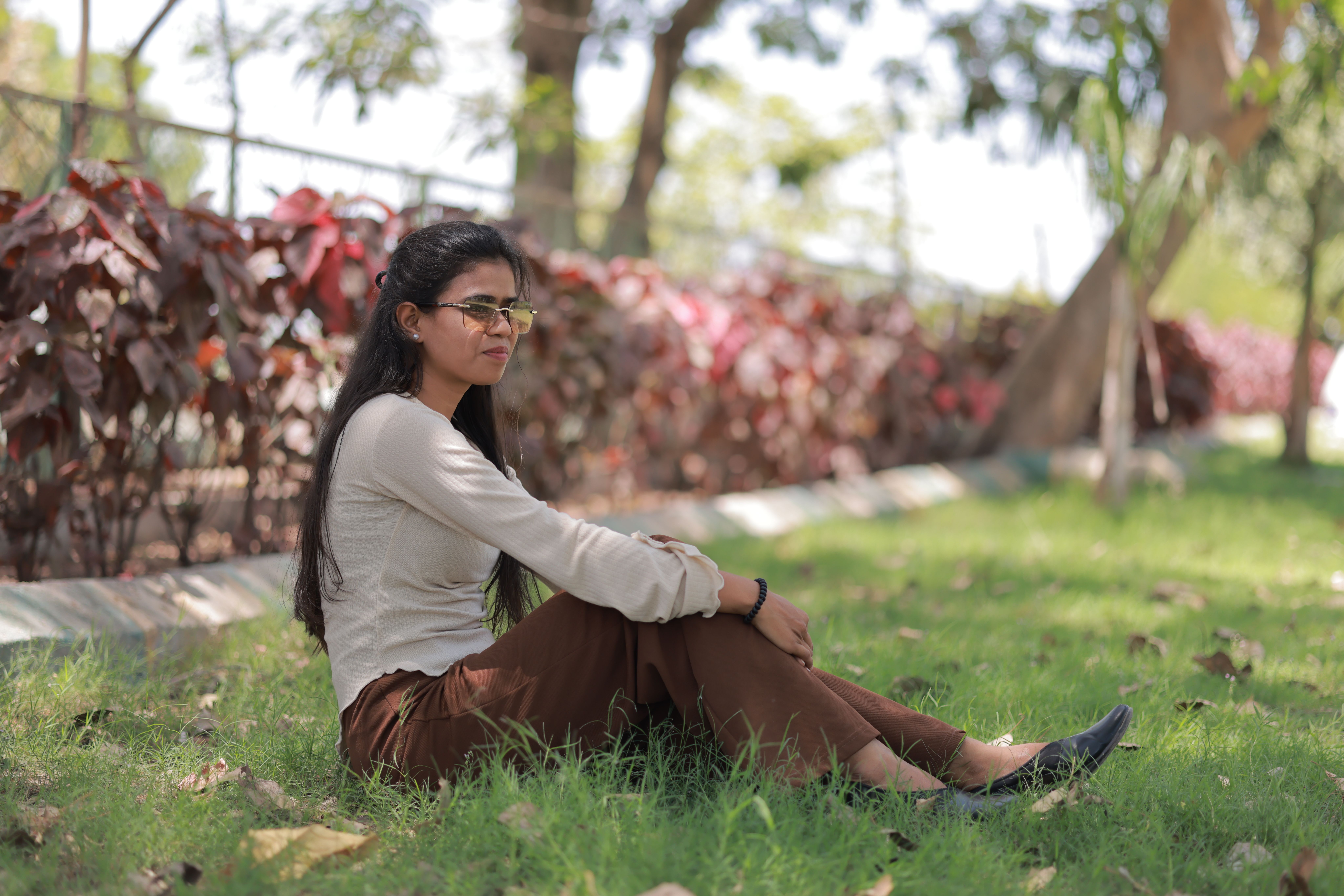 Young woman sitting on grass in the park, enjoying a sunny day outdoors with vibrant foliage.