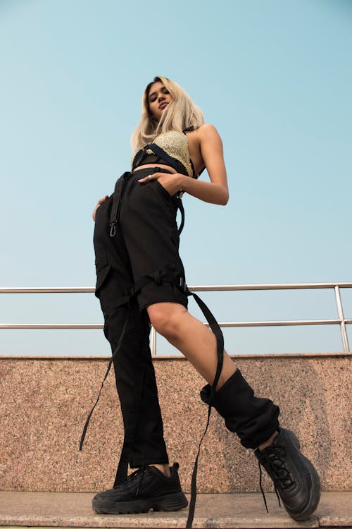 Photo Faible Angle De Femme Posant En Pantalon Noir Et Haut Doré Regardant Vers Le Bas