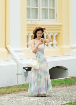 A woman in a summer dress uses her smartphone outside a yellow building.