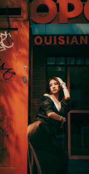 Stylish woman poses against a brick wall in a city setting with dramatic shadows.