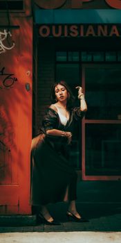 Fashionable woman in elegant dress posing in urban setting with vintage feel.