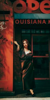 Fashionable woman leans against a red building in urban setting, exuding confidence and style.