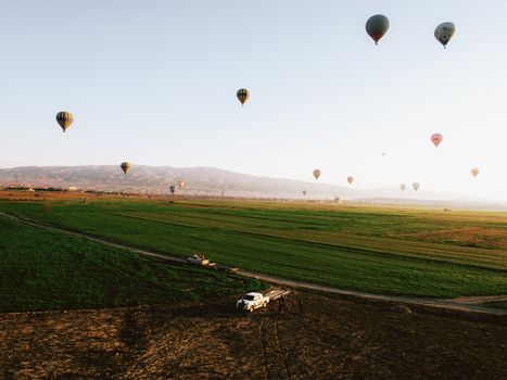 Colorful hot air balloons drift over expansive green fields at sunrise.