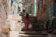A woman carrying bags climbs old stone steps in a colorful, narrow Cairo street.