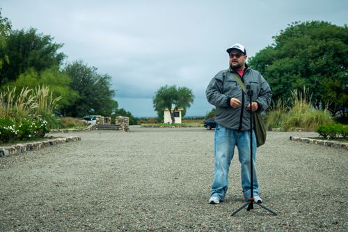 Free Bearded man with tripod stands in an outdoor park on a cloudy day. Stock Photo