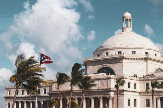 Stunning shot of Puerto Rico's Capitol with palm trees and flag under a bright blue sky.