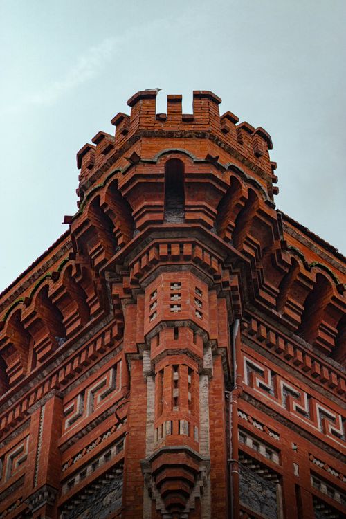 Free Close-up of a historic red brick tower's architectural details, under a cloudy sky. Stock Photo