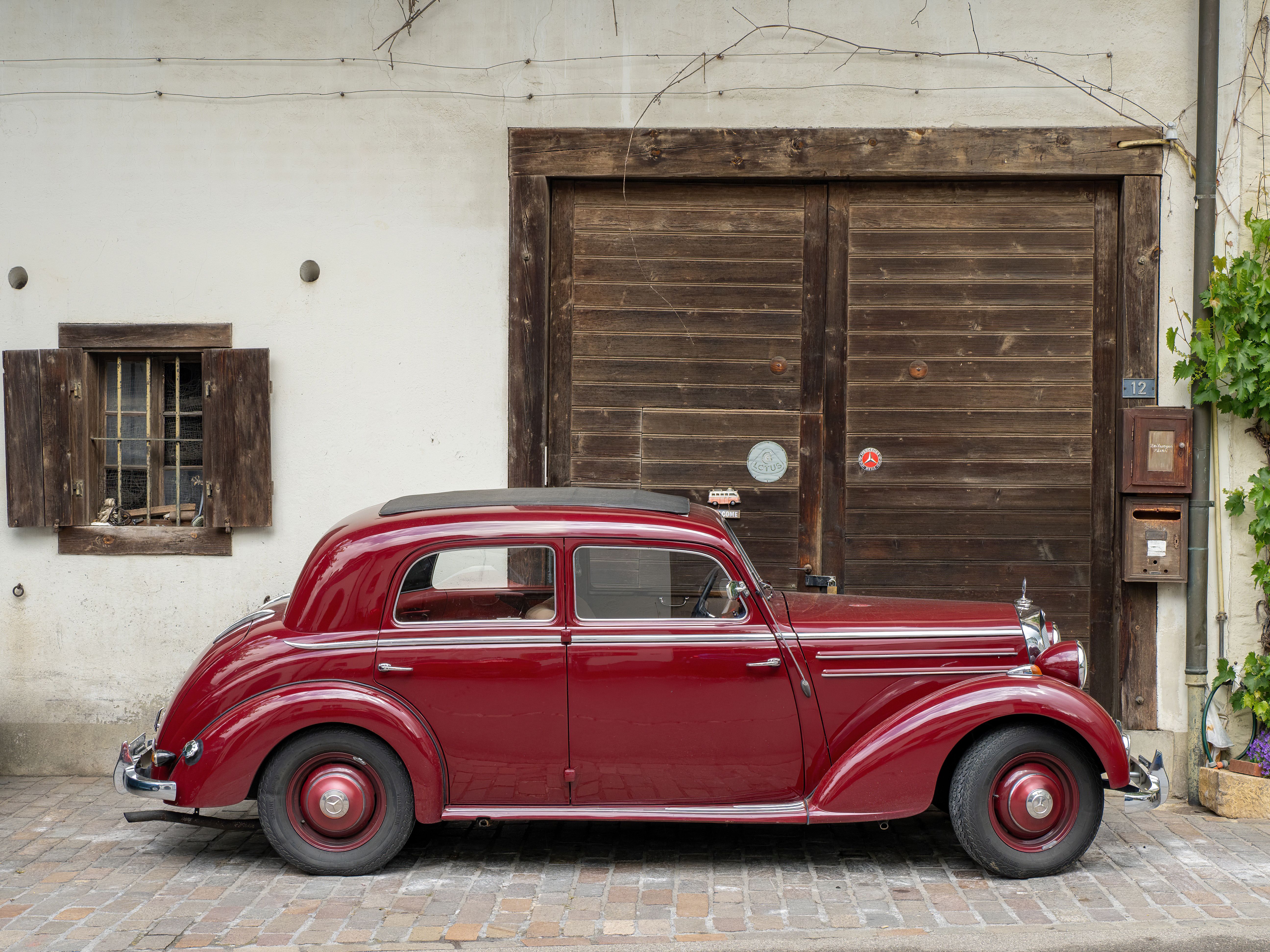 A beautifully preserved classic red car parked beside a rustic building, showcasing vintage charm.