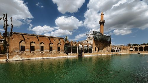 Free Scenic view of a historic mosque beside a green pool with cloudy sky, creating a serene and picturesque atmosphere. Stock Photo