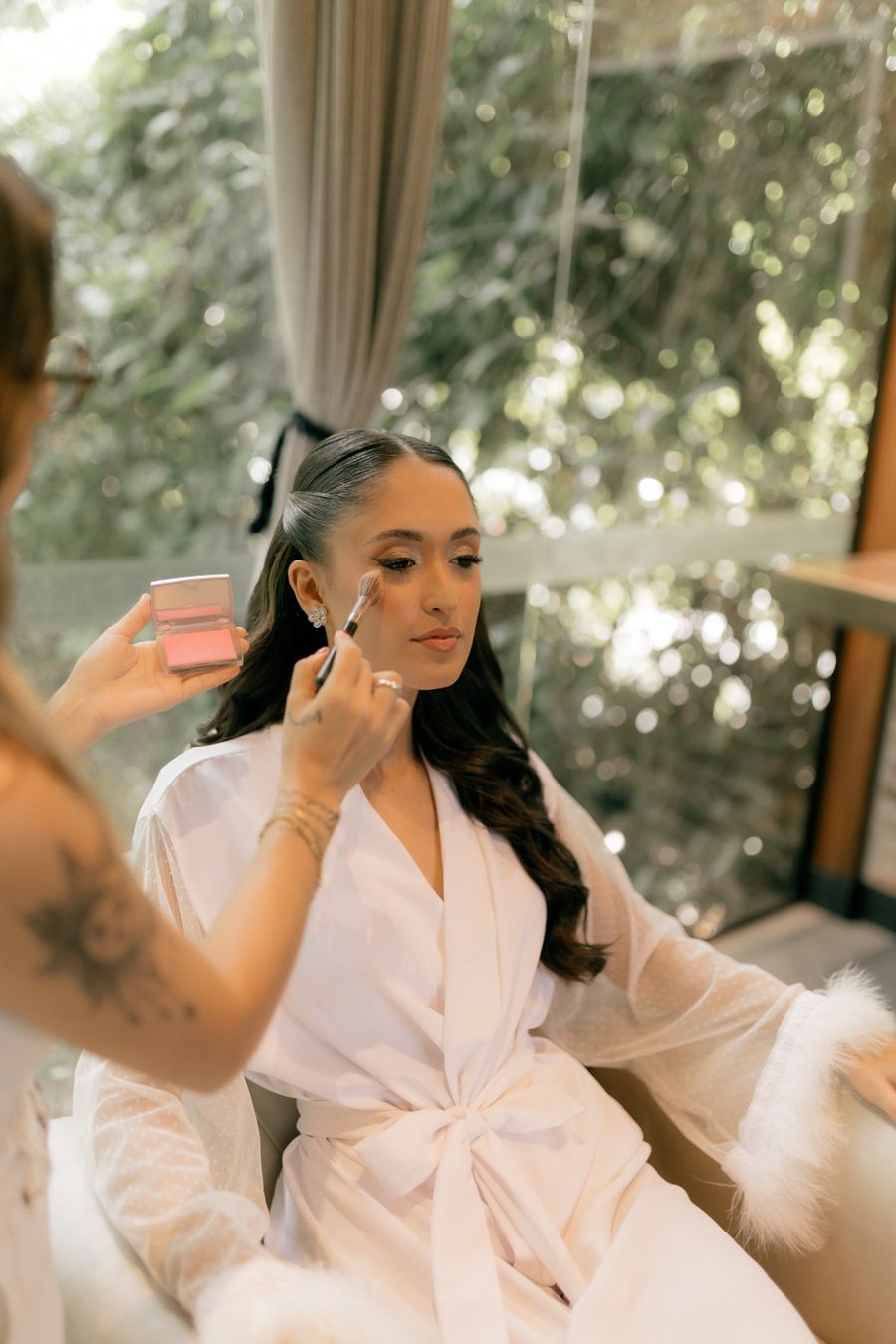 Makeup artist applying bridal makeup to a client in soft natural light