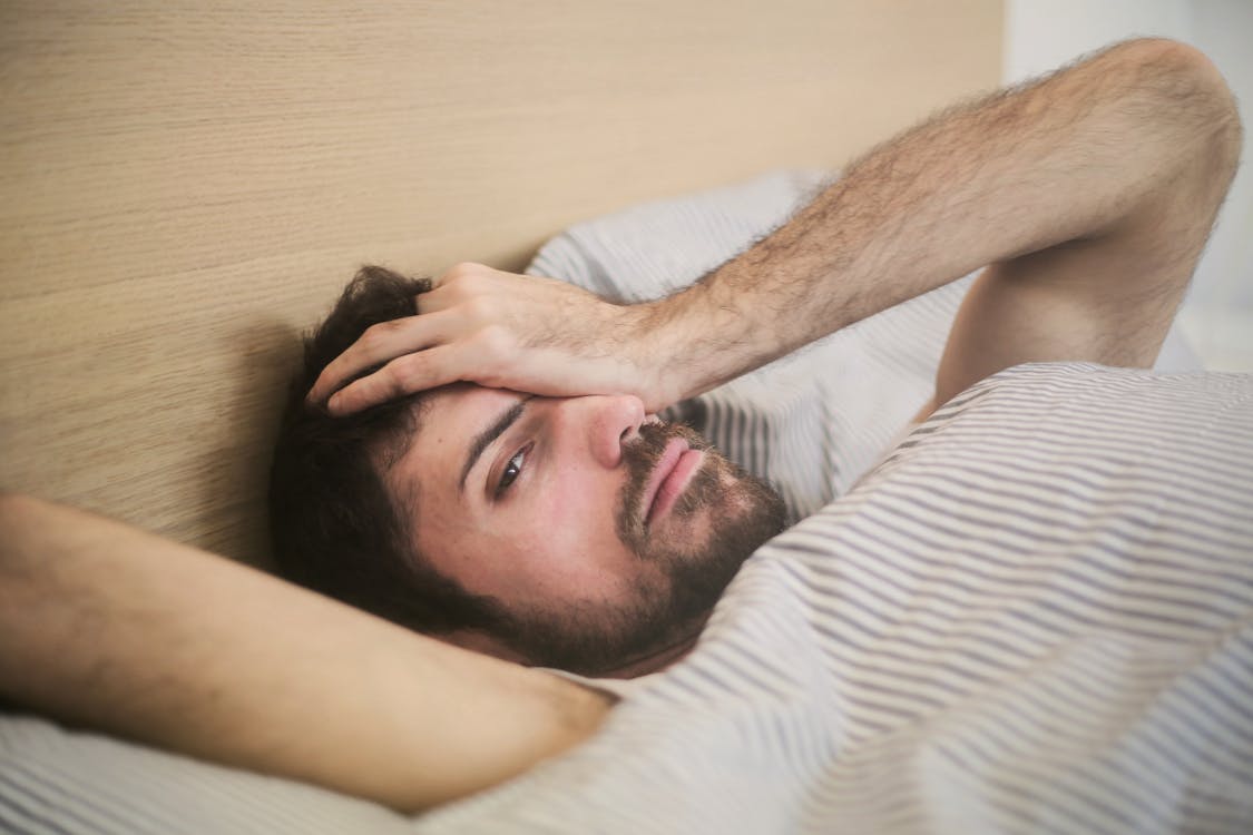 Free From above of sleepy bearded man just awakened rubbing eyes while lying on bed at home Stock Photo