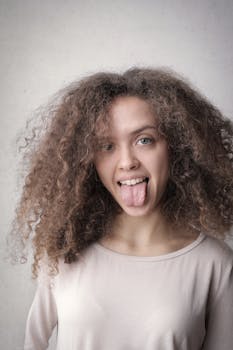 浅色背景前，一位卷发俏皮的女人露出有趣的面容