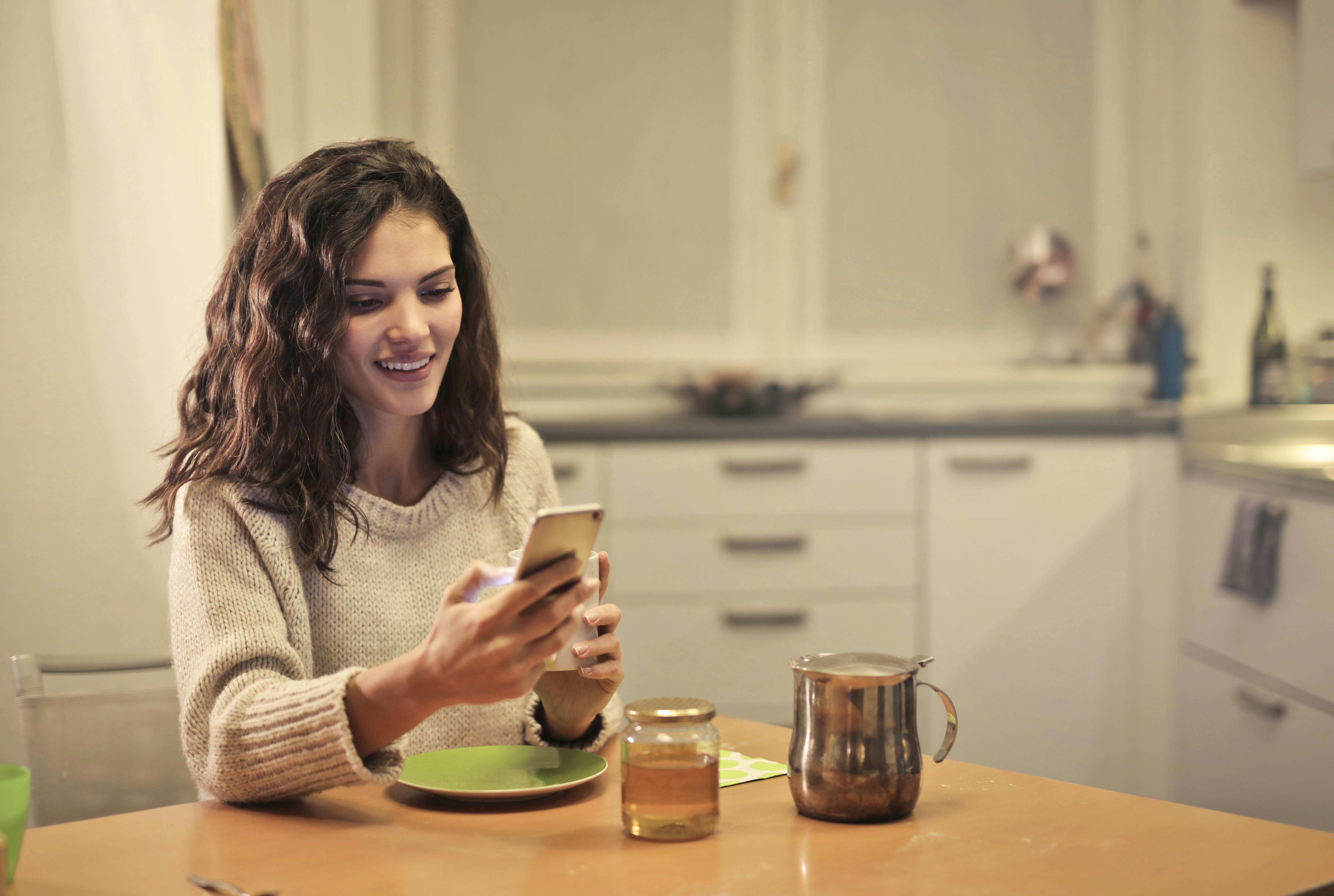 young woman drinking tea and using smartphone