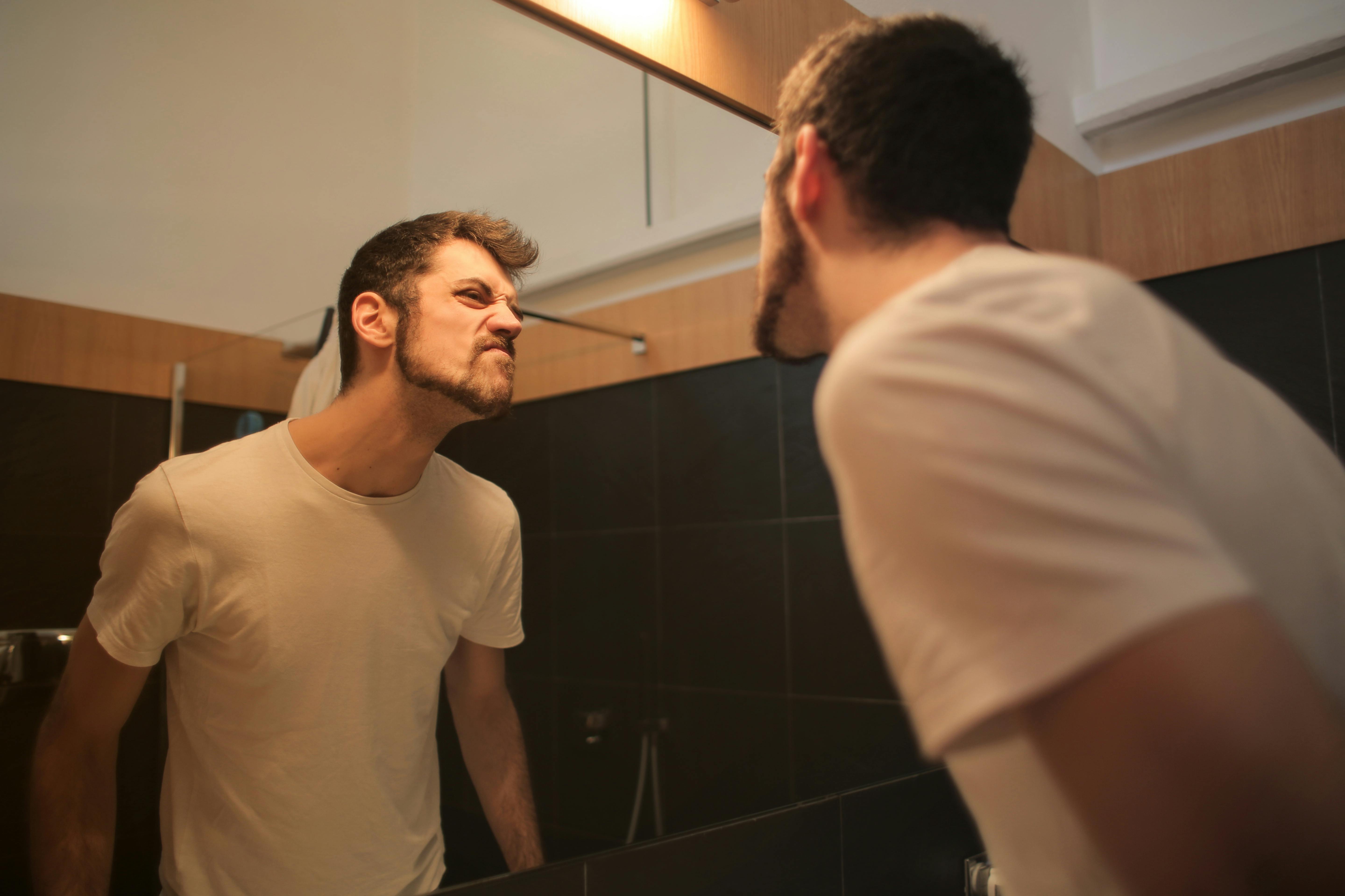 young unshaven man looking at mirror in bathroom