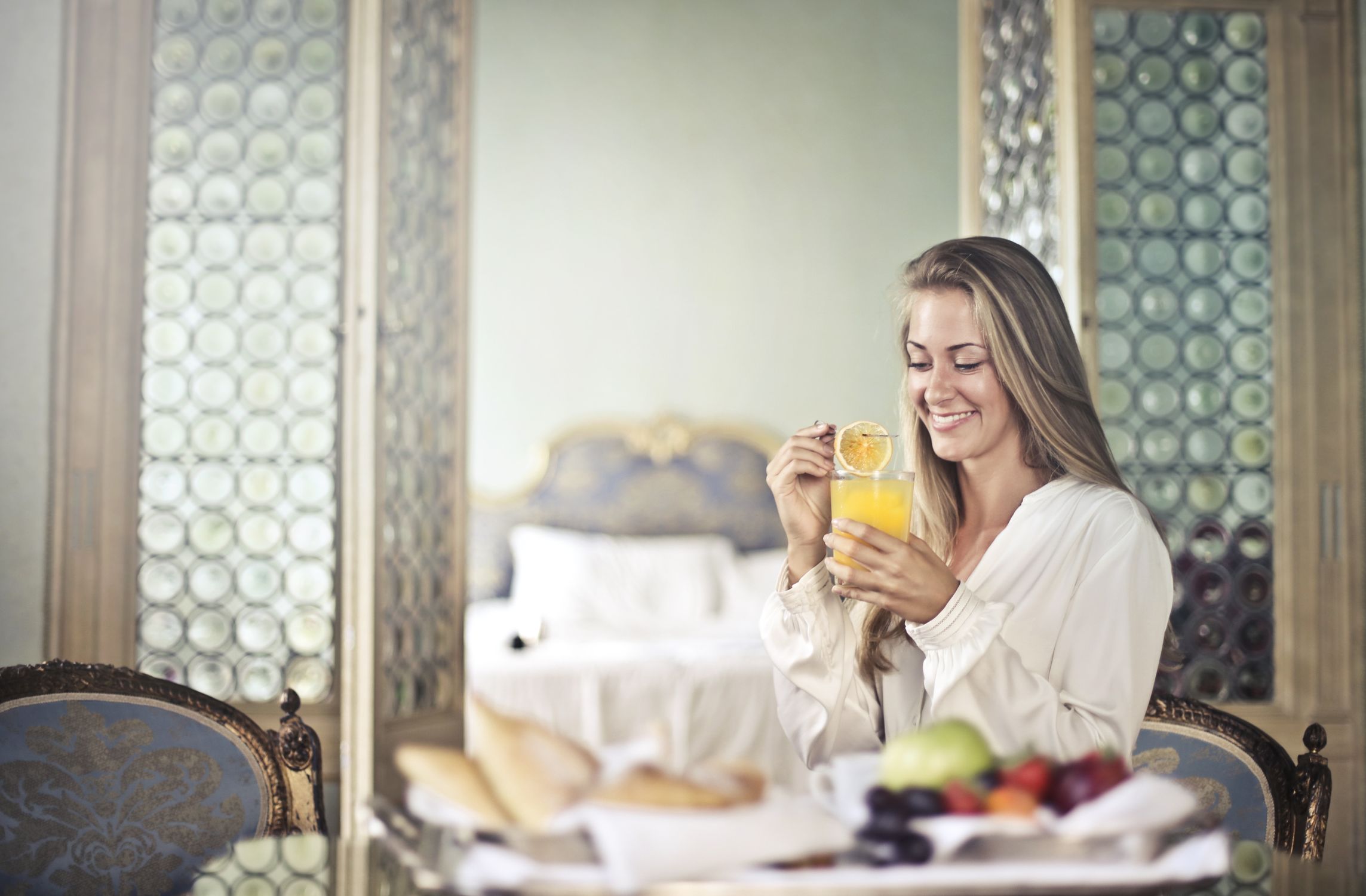 Side view of happy young female sitting at table with glass of fresh juice and enjoying delicious healthy breakfast in cozy room of hotel