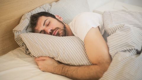 Man sleeping peacefully on striped bedding, embracing relaxation and comfort.
