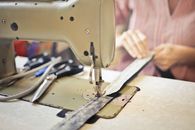 Crop craftswoman in casual wear sitting at old fashioned sewing machine and stitching pieces of fabric while working in workshop