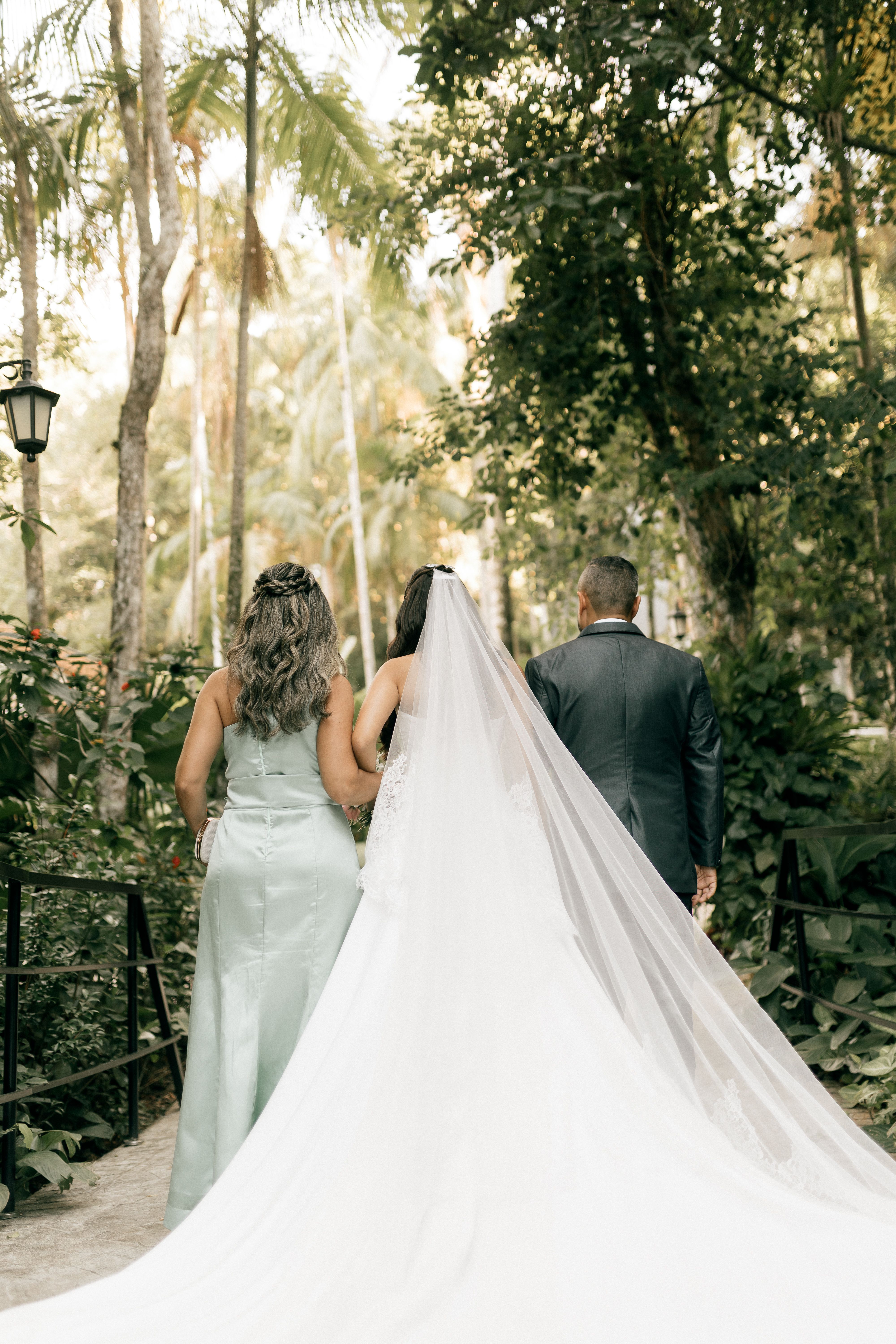 Bride walking with parents in a lush garden setting, elegant outdoor wedding with flowing gown.