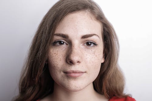 Close-up Photo of Freckled Woman in Red Top IN Front Of White Background