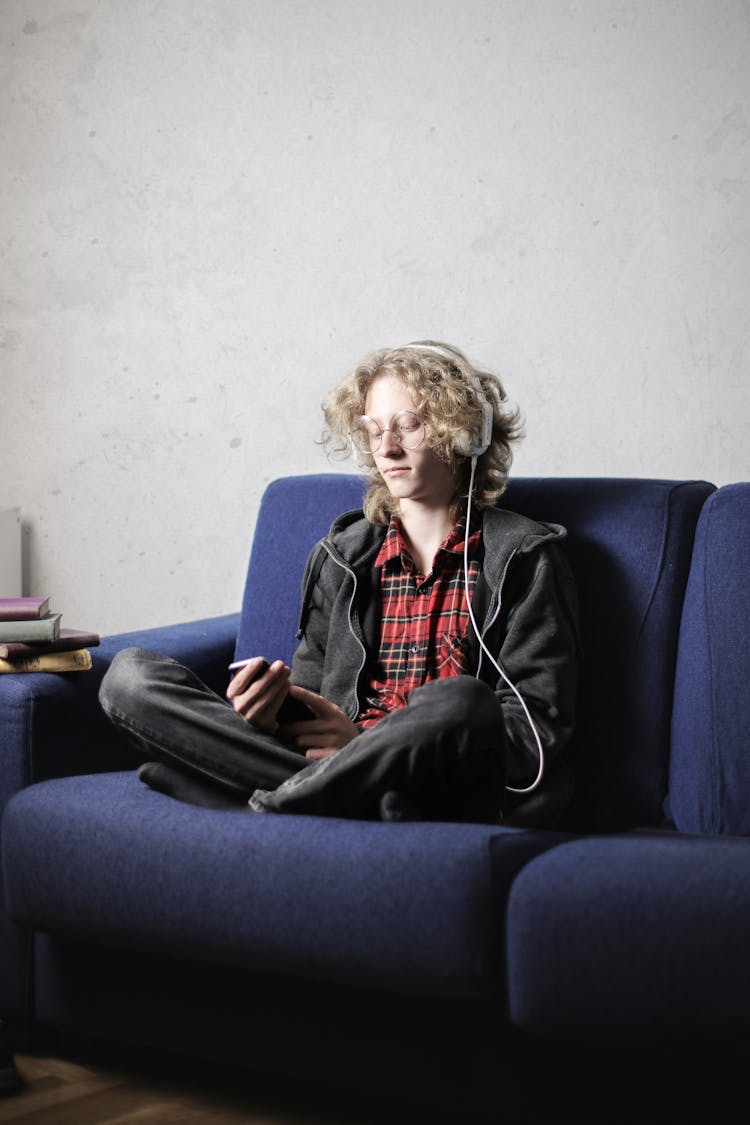 Photo Of Person In Black Hoodie With Headphones On  Sitting On Blue Sofa