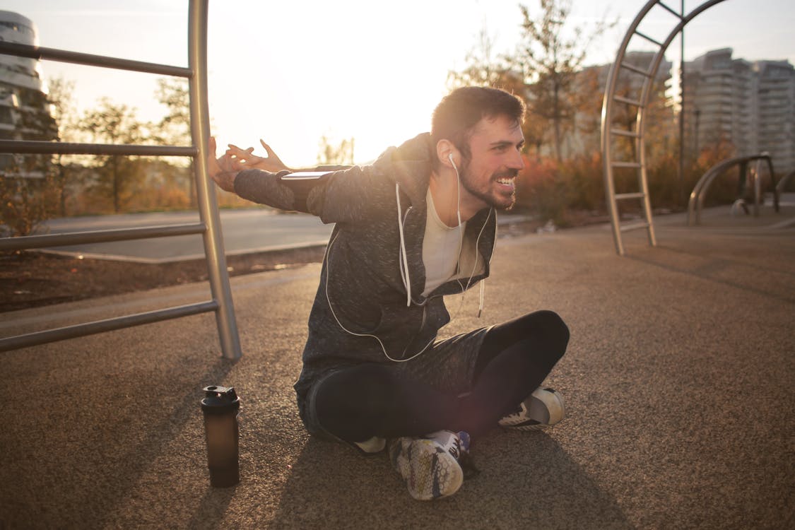 Cheerful athletic man stretching arms on sports ground