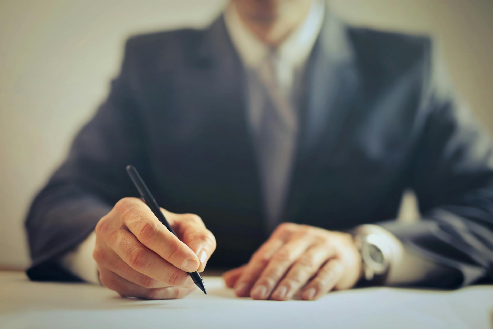 Faceless businessman in suit signing a contract at office desk, focused on task.