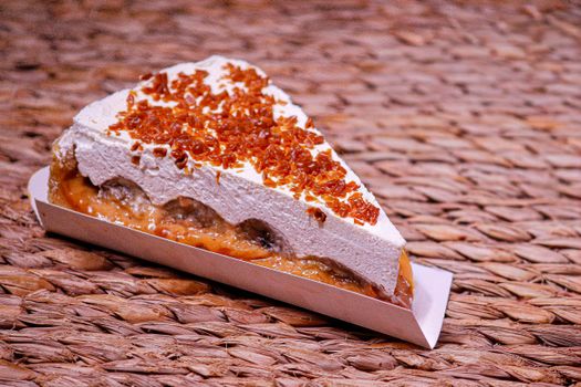 Tantalizing slice of banoffee pie topped with cream and caramel, set on a wicker mat.