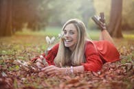 身着红色连衣裙的微笑女子躺在公园的秋叶上，享受着这个季节