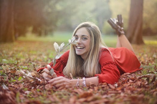 一位身穿红色连衣裙的女子微笑着躺在公园的秋叶上，享受着这个季节