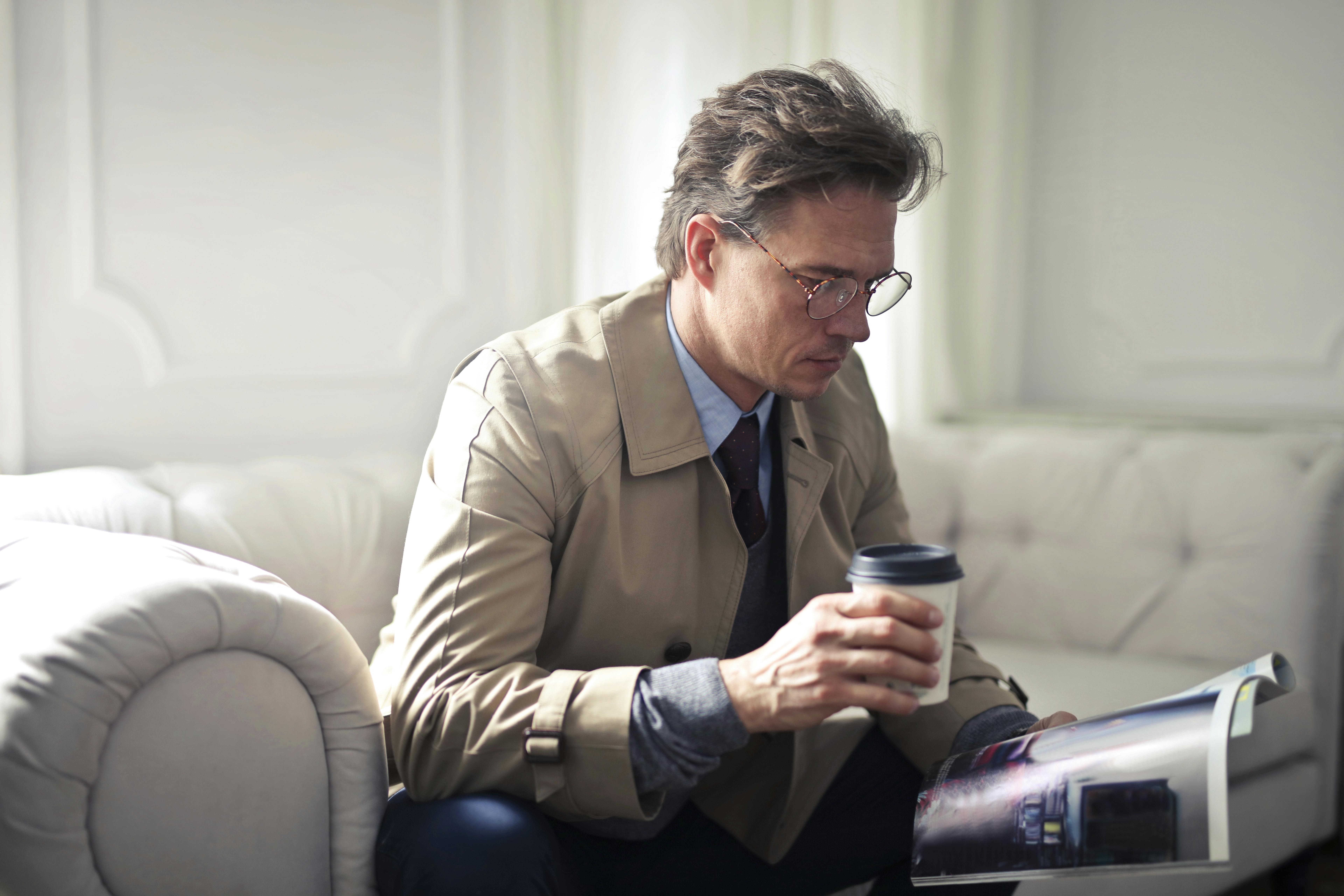 concentrated businessman with takeaway coffee reading magazine in living room