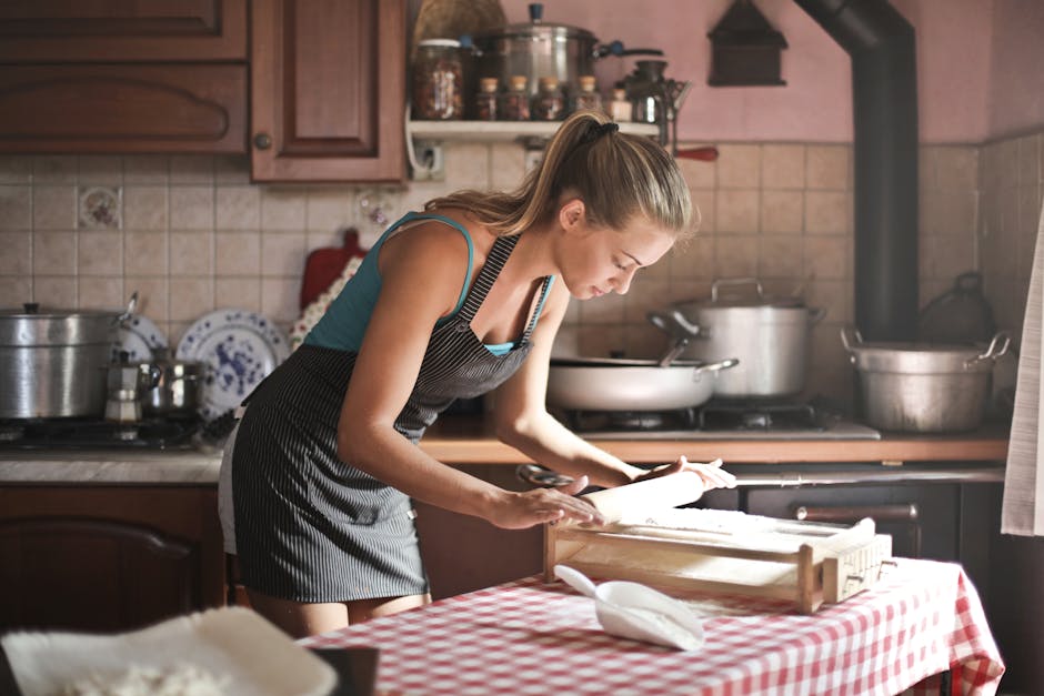 Afbeelding van Side view of huisvrouw met schort die aan tafel staat in gezellige keuken en deeg voor het bakken klaarmaakt met behulp van de deegroller