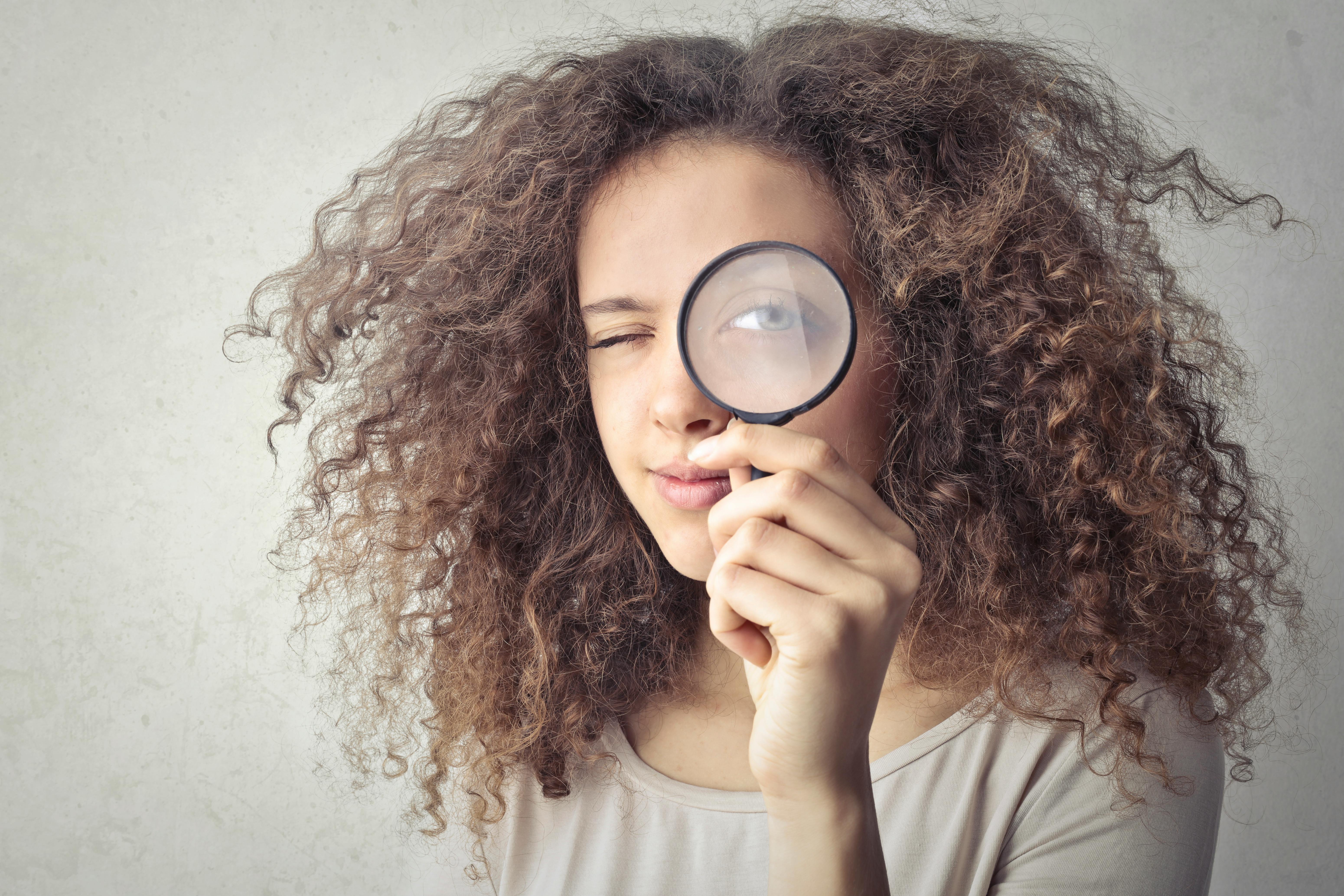 portrait photo of woman holding up a magnifying glass over her eye