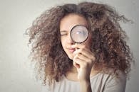 Portrait Photo of Woman Holding Up a Magnifying Glass Over Her Eye