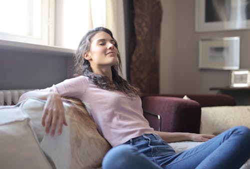 Free Photo of Woman in Pink Long Sleeve Shirt and Blue Denim Jeans Sitting on Brown Sofa with Her Eyes Closed Stock Photo
