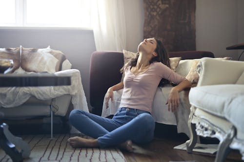 Free Photo of Woman in Pink Long Sleeve Top and Blue Denim Jeans Sitting on the Floor While Leaning Against a Purple Sofa with Her Eyes Closed Stock Photo
