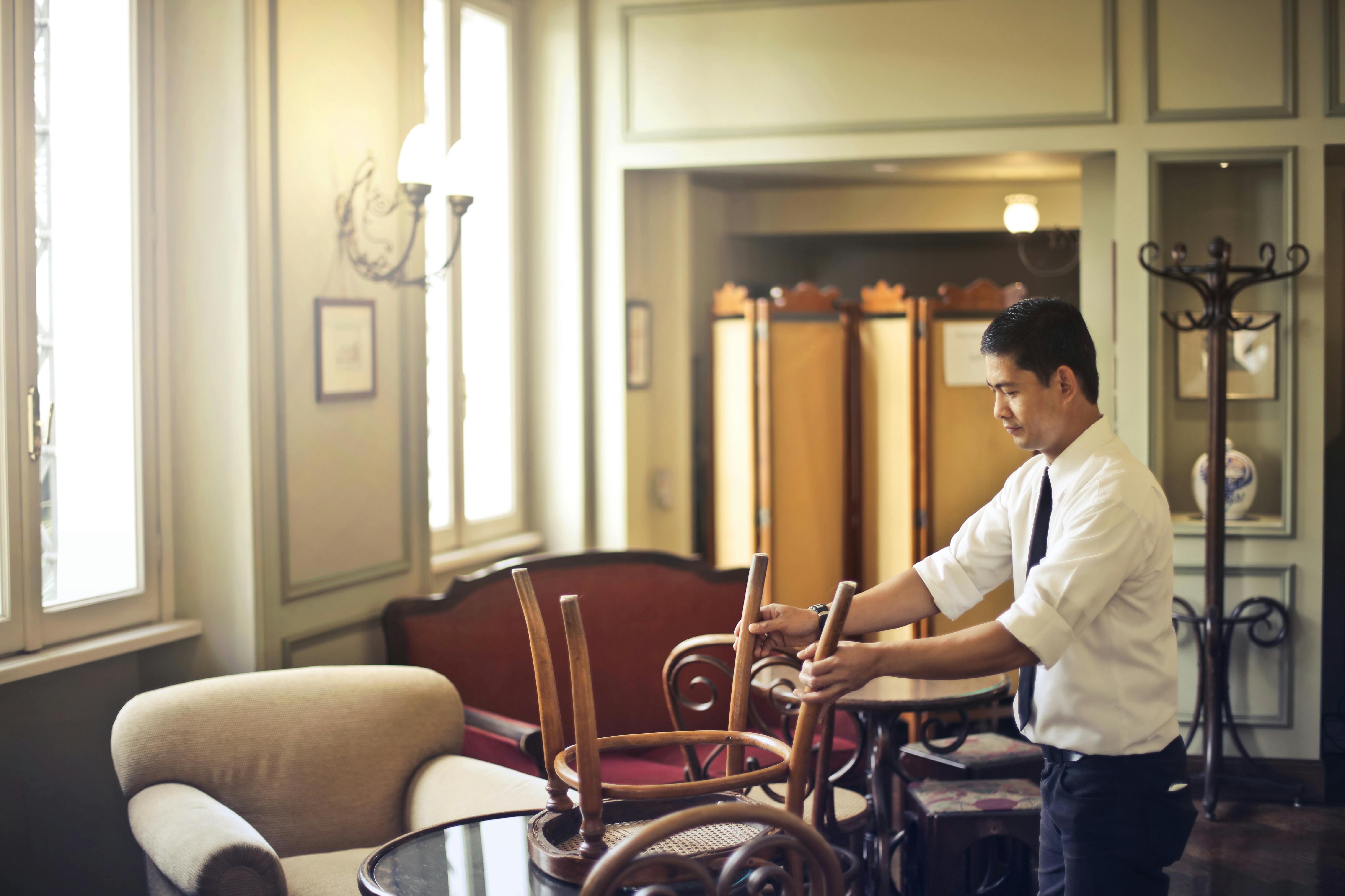 Ethnic male restaurant manager stacking chair on table after closing ...