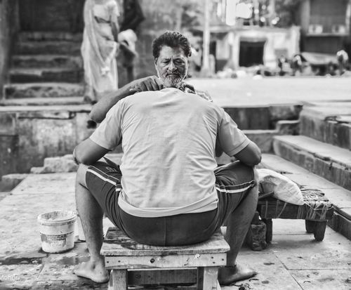 Free Black and white image of a street barber providing a haircut in a busy Indian street scene. Stock Photo