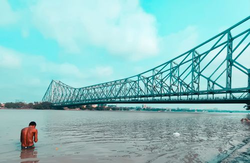 Free Man bathing in the Hooghly River with the iconic Howrah Bridge in the background, Kolkata. Stock Photo