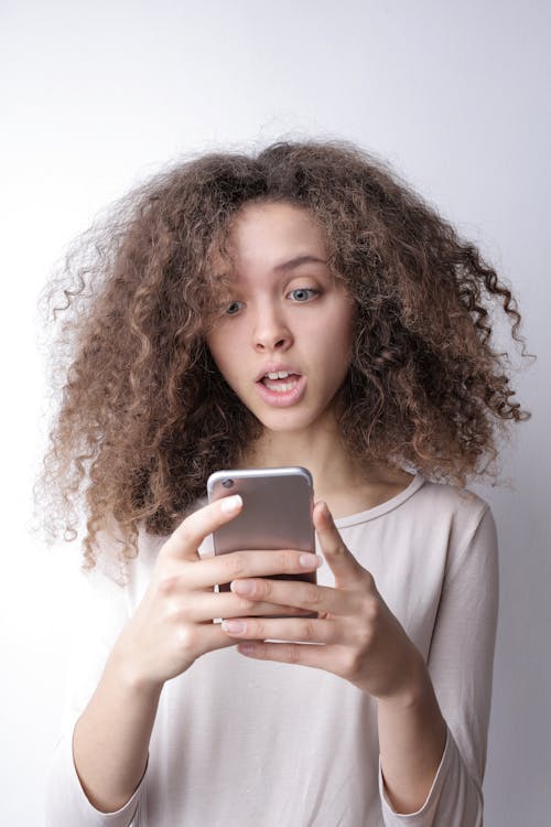 Gratis Wanita Muda Yang Terkejut Melihat Lihat Ponsel Foto Stok
