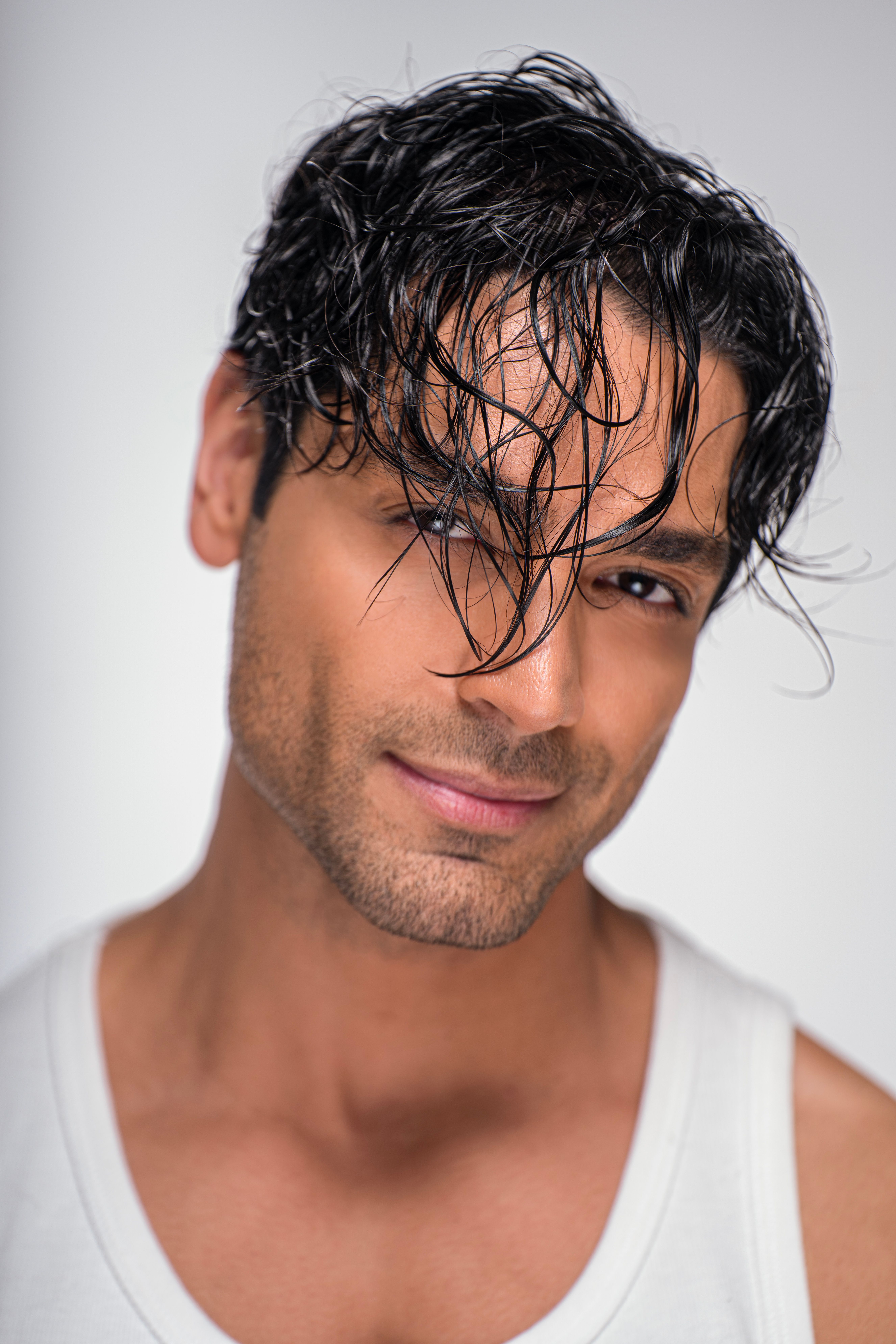 Close-up portrait of an adult man with wet hair wearing a white tank top against a neutral background.