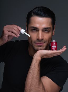 Confident man displaying facial serum with dropper in a professional studio setup, highlighting skincare routine.