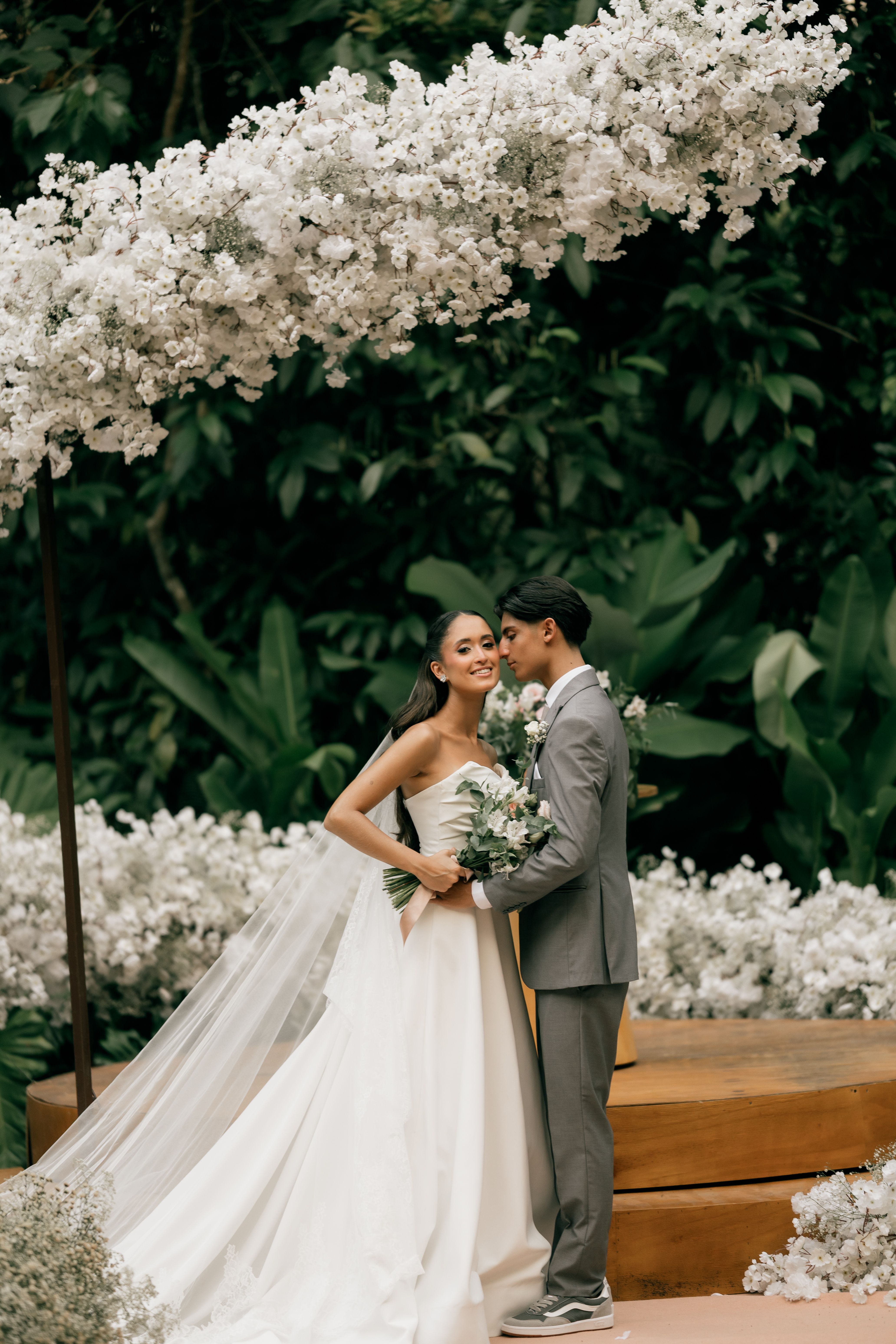 A beautiful outdoor wedding with a couple under a white floral arch.