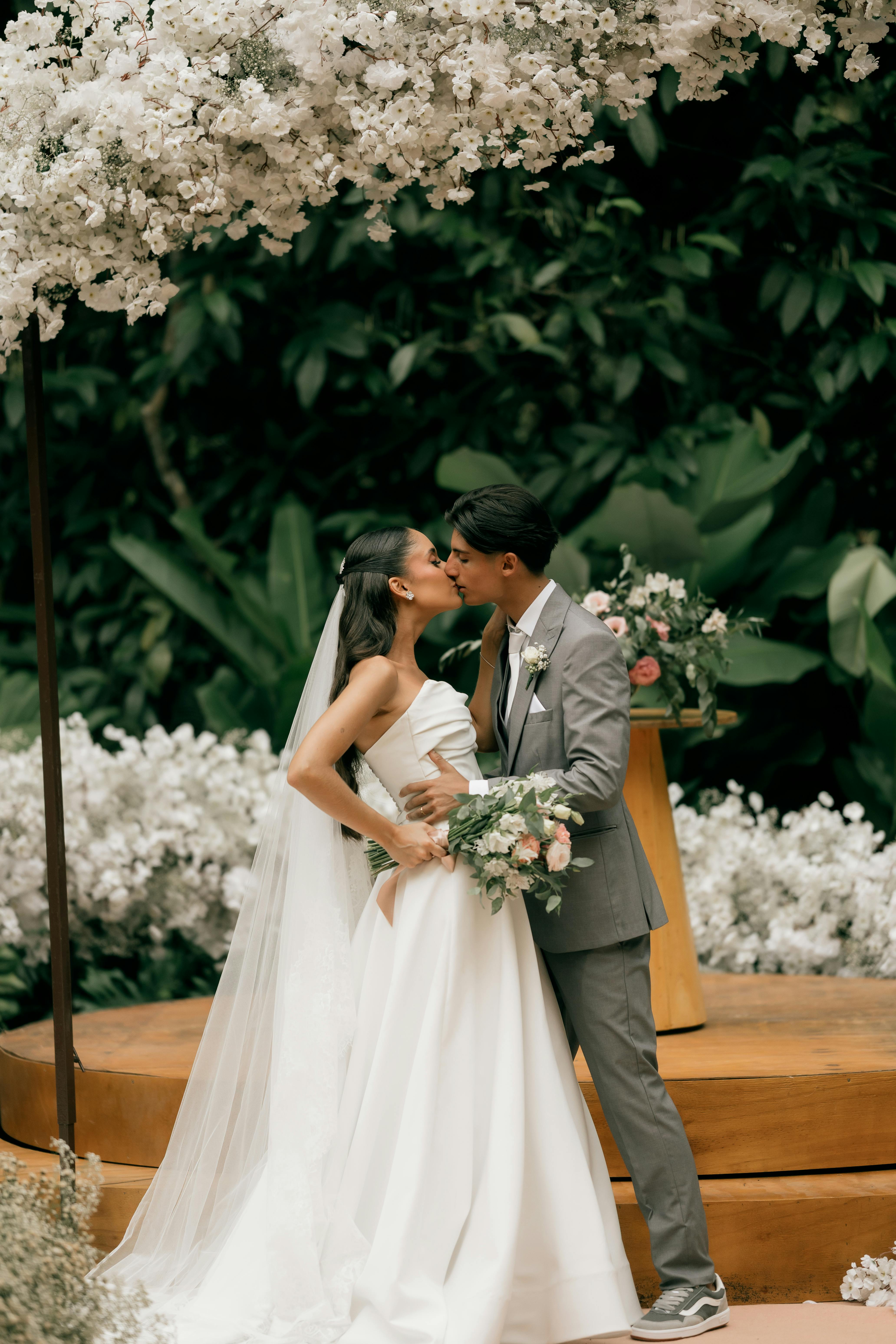 Bride and groom sharing a kiss under a flower arch in a lush outdoor setting.