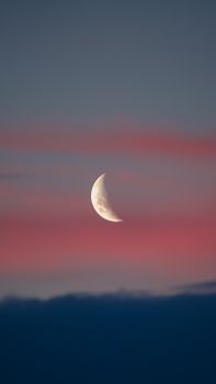 A serene crescent moon set against a vivid pink and blue twilight sky, creating a peaceful atmosphere.