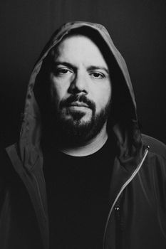 Black and white portrait of a man wearing a hooded jacket, conveying a mysterious and introspective mood.