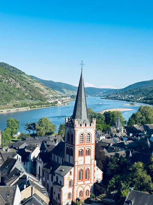 Free A picturesque aerial shot capturing a historic German church alongside the serene Rhine River under a clear blue sky. Stock Photo