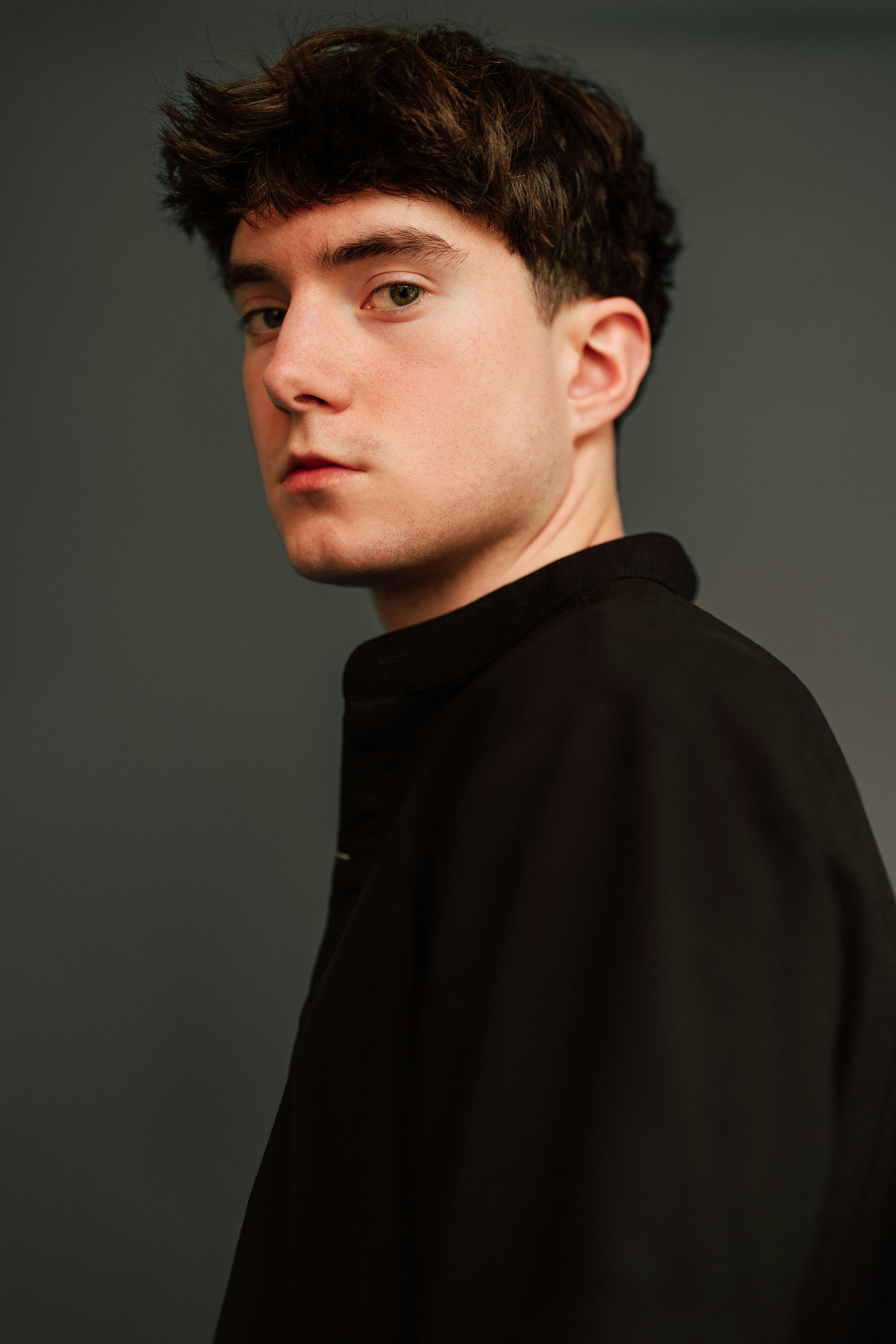 Moody portrait of a young adult male with a neutral background. Captures serious expression in soft lighting.