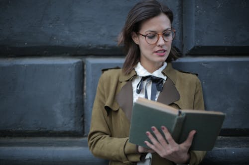 Photo of Woman in Brown Coat and Glasses Reading a Book 