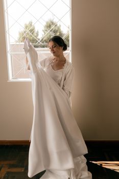 A bride holds her elegant wedding dress in a softly lit room, exuding a sense of anticipation and joy.