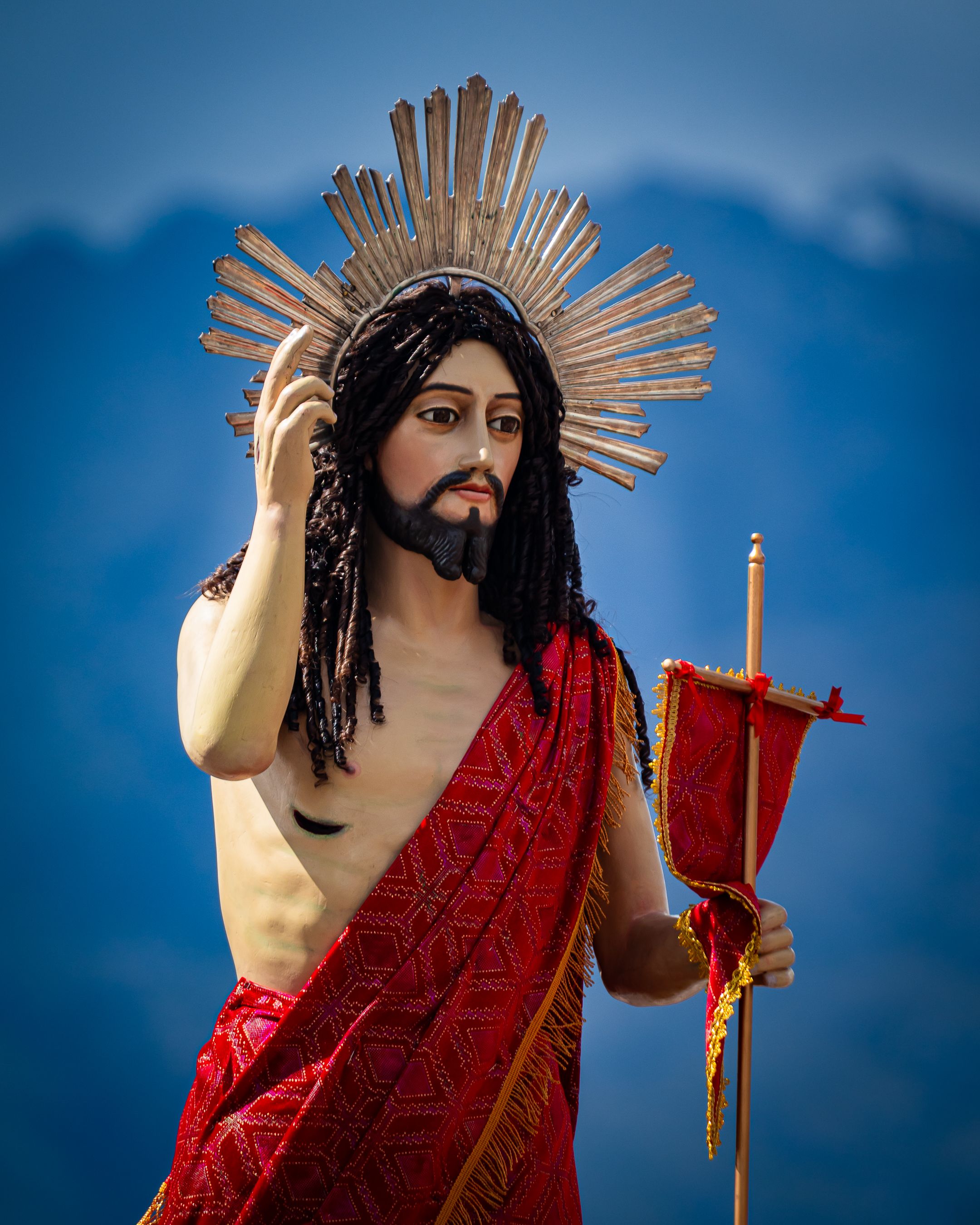 A statue of Jesus Christ adorned with a radiant halo against a mountain background, symbolizing faith.